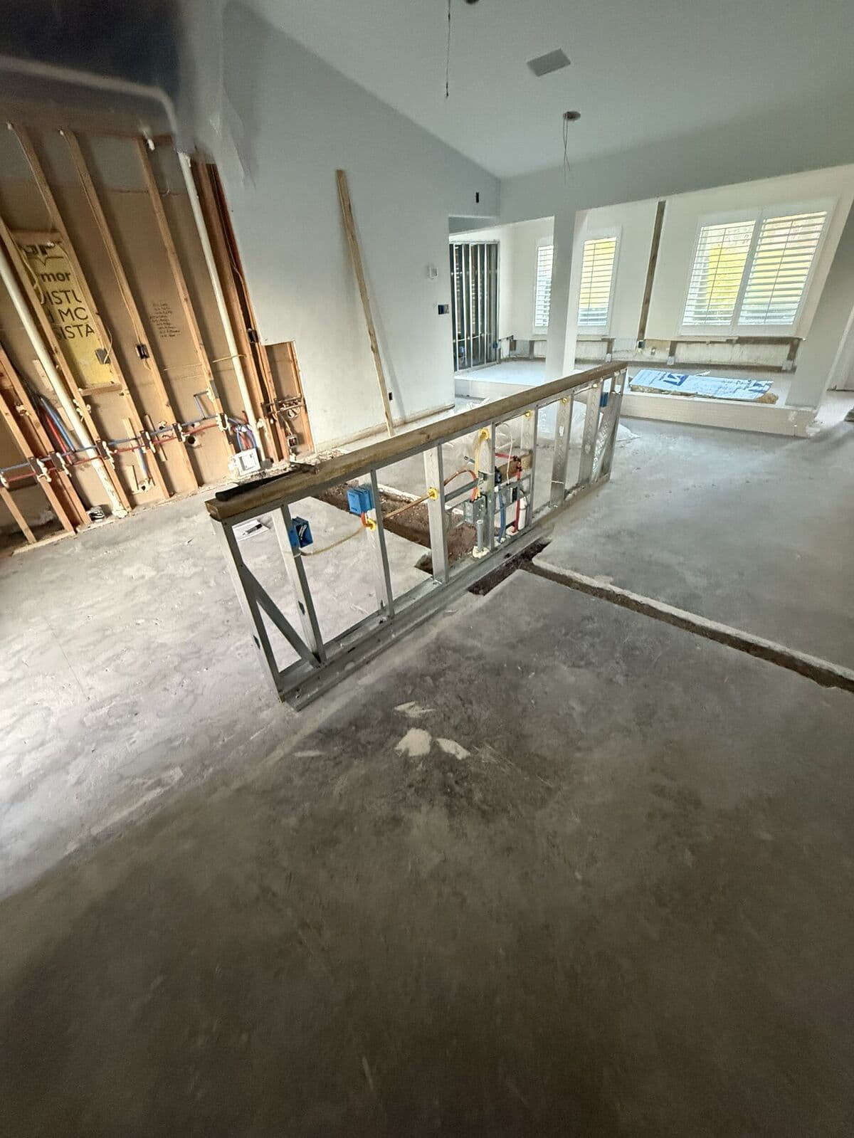 A trench cut across the slab beside exposed wall framing and plumbing lines